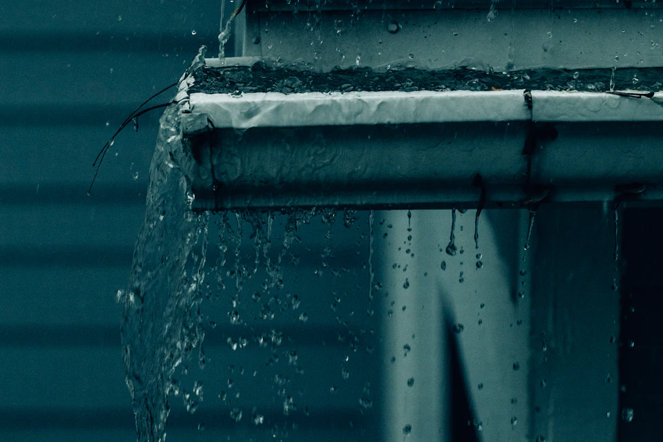 Canalón con una fuga desbordando agua contra la fachada en plena lluvia